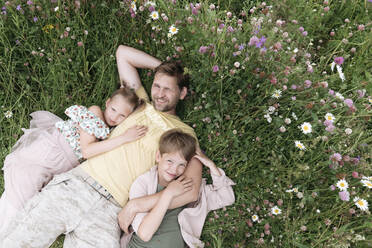 Lächelnder Vater mit Kindern, die auf dem Boden inmitten von Blumen liegen - EYAF01220