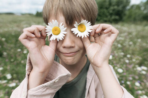Close-up of boy hiding eyes with chamomile flowers stock photo