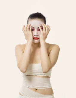 Junge Frau verschmiert Opern-Make-up, während sie vor einem weißen Hintergrund steht - EAF00024