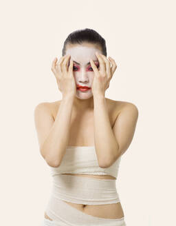 Young woman smudging opera make-up while standing against white background - EAF00024