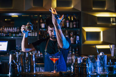 Männlicher Barkeeper bei der Herstellung von Cocktails an der Theke in einer Kneipe bei Nacht - OCMF01571
