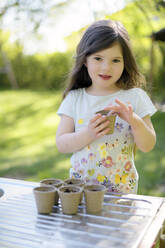 Nettes Mädchen pflanzt Samen in kleinen Töpfen auf einem Tisch im Garten - BRF01466