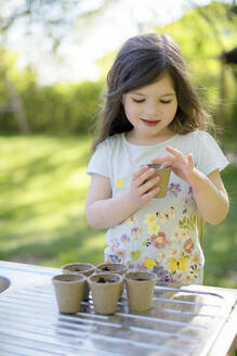 Nettes Mädchen pflanzt Samen in kleinen Töpfen auf dem Tisch im Garten - BRF01467