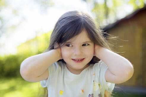 Cute girl covering ears at yard during sunny day - BRF01468