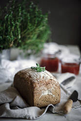 Delicious fresh aromatic rye bread on napkin near knife and cans with tomatoes homemade jam on blurred background - ADSF04272