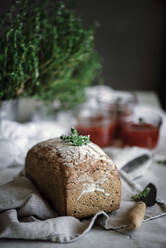 Köstliche frische aromatische Roggenbrot auf Serviette neben Messer und Dosen mit Tomaten hausgemachte Marmelade auf unscharfen Hintergrund - ADSF04277