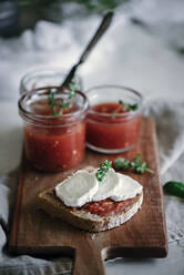 Von oben Sandwich von Scheibe frischem Roggenbrot mit Käse und Kräutern in der Nähe von Dosen mit Tomaten hausgemachte Marmelade auf Schneidebrett auf unscharfen Hintergrund - ADSF04279