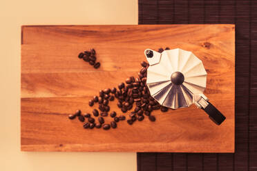 Geröstete Kaffeebohnen liegen auf einem Holzbrett neben einer Metallkanne auf einem Tisch - ADSF04374
