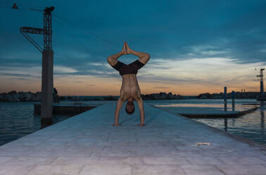 Junge shirtless Sportler tun Handstand auf Pier in der Nähe von Wasser in den Abend mit erstaunlichen Himmel - ADSF04501