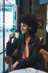 Schwarze Frau mit Afro-Haar trinkt einen Kaffee in einem Café - ADSF04502