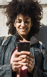 Portrait of black woman with afro hair leaning on a wall in the street - ADSF04508