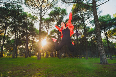 Fröhliche Frau in sportlichem Outfit springt hoch über eine grüne Wiese in einem sonnigen Park - ADSF04619