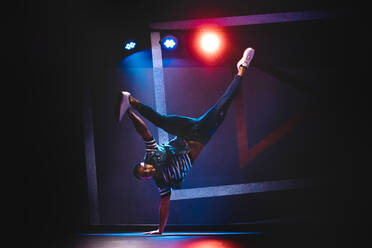 Modern ethnic man in denim and white sneakers showing contemporary dance in handstand position - ADSF04627