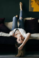 Excited young woman smiling while lying on soft couch in stylish room - ADSF04645