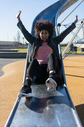 Woman with afro hair jumping down a slide with great joy - ADSF04690