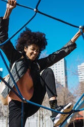 Woman with afro hair climbing by children's attractions in a park - ADSF04693