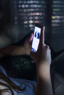 Teenage girl in sleepwear looking at her smartphone in her room in the afternoon - ADSF04700