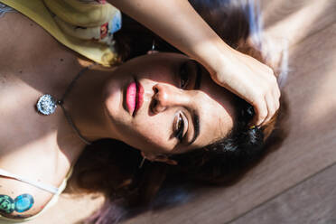 From above shot of seductive young lady looking at camera and touching hair while lying on lumber floor - ADSF04801