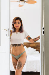 Red-haired tattooed woman in lingerie at home near the window