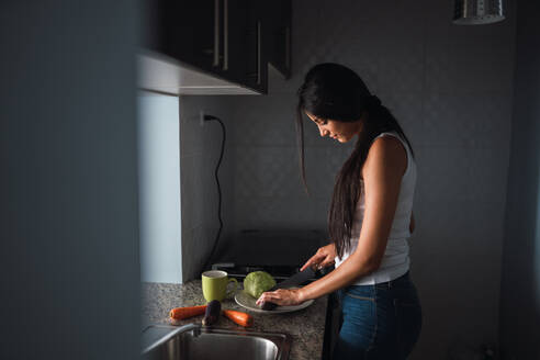 Schöne leidenschaftliche Brünette Hispanic Frau Schneiden von Gemüse in der modernen Küche - ADSF04831