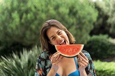 Verspielte junge Frau isst Wassermelone im Garten - AFVF06814