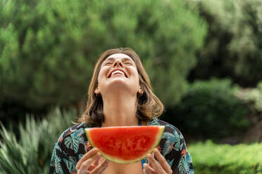 Fröhliche junge Frau hält Wassermelonenscheibe im Hof - AFVF06815