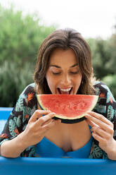 Glückliche junge Frau isst Wassermelone im aufblasbaren Schwimmbad im Garten - AFVF06816