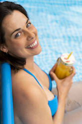Glückliche Frau hält Orangensaft im aufblasbaren Schwimmbad im Hof - AFVF06820