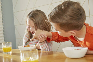 Boy and girl sitting at kitchen table, eating breakfast. - CUF56162