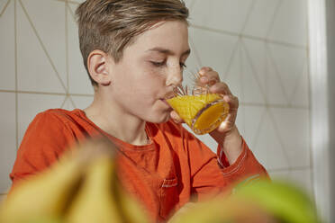 Junge sitzt am Frühstückstisch und trinkt Orangensaft. - CUF56163