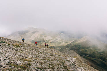 Rückenansicht einer Gruppe von Reisenden, die an einem nebligen Tag entlang eines beeindruckenden Bergrückens wandern - ADSF04847