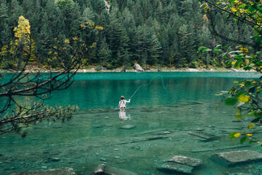 Back view of man standing in clean water of beautiful lake and fishing - ADSF04869