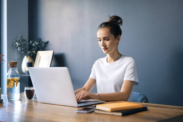 Selbstbewusste Geschäftsfrau mit Laptop auf dem Schreibtisch an der Wand im Heimbüro - BSZF01574