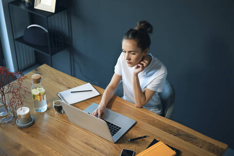 Serious female entrepreneur using laptop on desk while sitting in home office stock photo