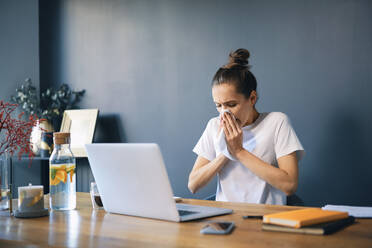 Geschäftsfrau schnäuzt sich die Nase, während sie am Schreibtisch im Home Office sitzt - BSZF01583