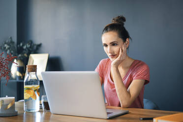 Female entrepreneur using laptop on desk against wall in home office - BSZF01584