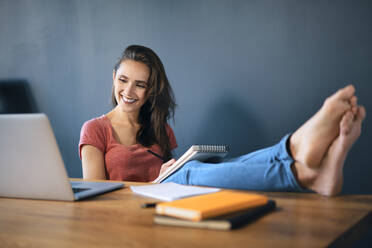 Smiling female entrepreneur with feet up on desk working in home office - BSZF01588