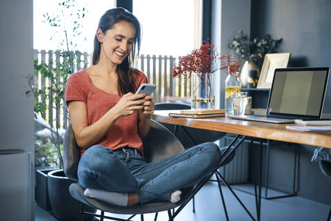 Female entrepreneur using smart phone while sitting on chair by desk in home office stock photo