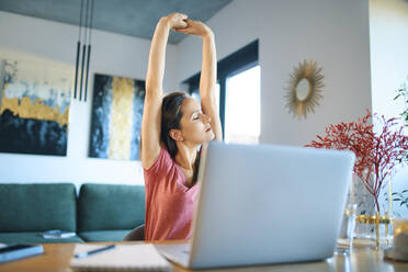 Tired female freelancer stretching arms while sitting in home office - BSZF01597