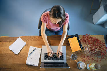 Freiberuflerin, die im Home-Office über einem Laptop auf dem Schreibtisch sitzt - BSZF01599
