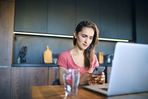 Freiberuflerin, die am Schreibtisch im Home Office sitzt und ein Mobiltelefon benutzt - BSZF01602