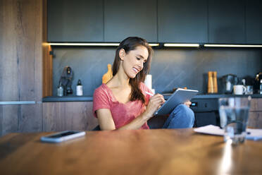 Lächelnde Unternehmerin, die ein digitales Tablet benutzt, während sie am Schreibtisch im Heimbüro sitzt - BSZF01604