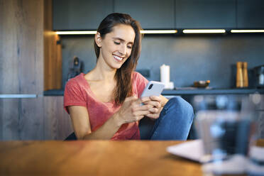 Lächelnde Unternehmerin, die ein Smartphone benutzt, während sie am Schreibtisch im Home Office sitzt - BSZF01605