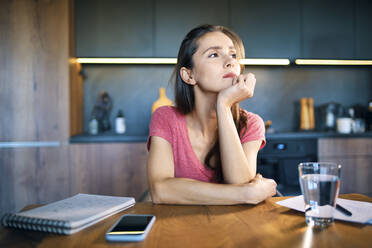 Thoughtful female entrepreneur looking away while sitting at desk in home office - BSZF01608