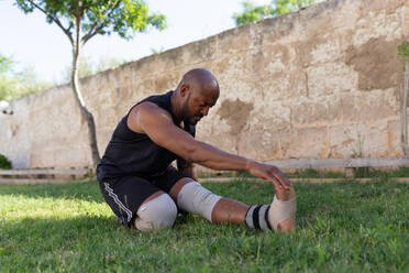 Mature man with shaved head exercising on grassy land against wall in yard - JPTF00568