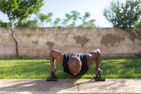 Mature man with shaved head practicing push-ups on grassy land in yard stock photo