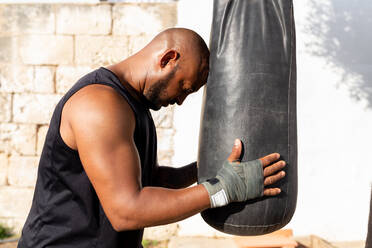 Bald mature man holding punching bag while standing in yard - JPTF00577