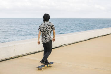 Junger Mann auf dem Skateboard auf der Promenade am Meer in der Stadt - XLGF00393