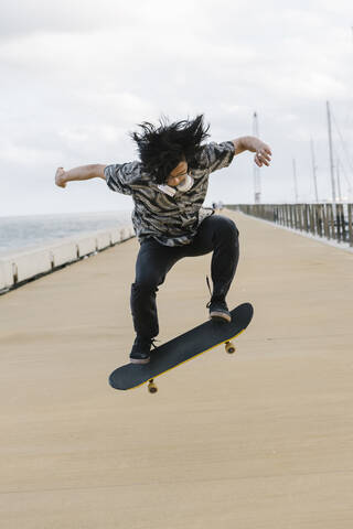 Young man with skateboard performing stunt on promenade against sky stock photo