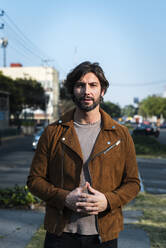 Handsome man wearing jacket standing on street against clear sky in city - JMPF00242